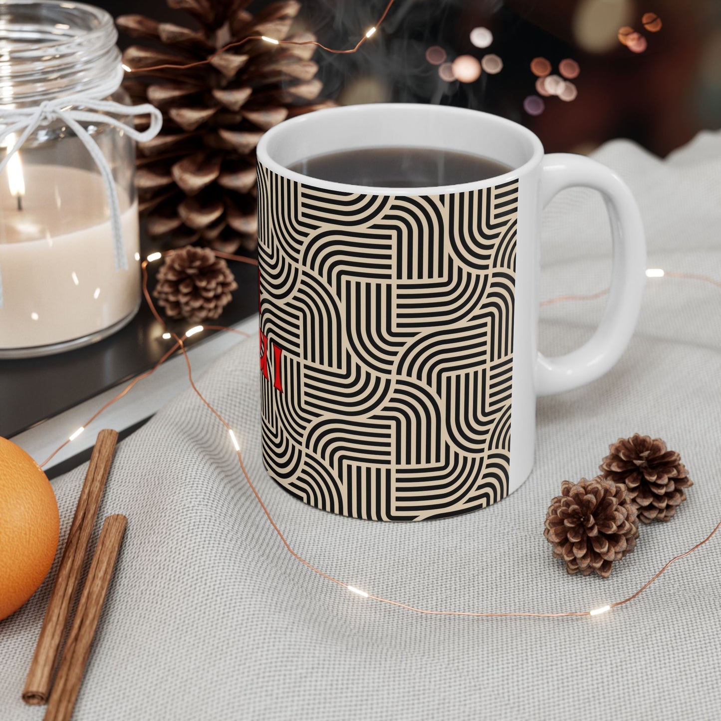 White mug with black geometric pattern on a table with candles, oranges, and pinecones.