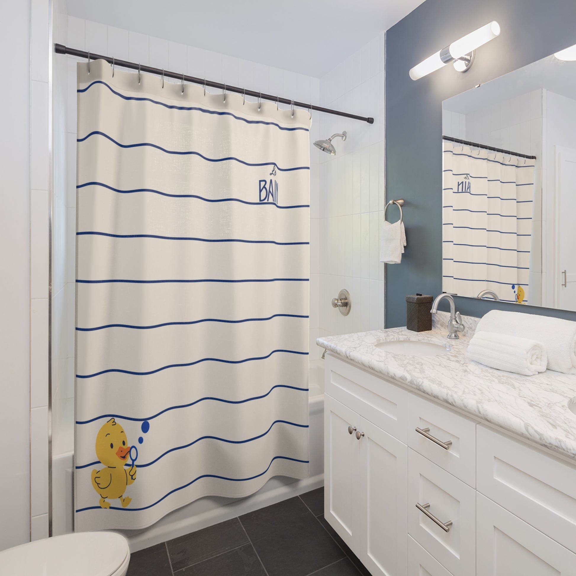A bathroom scene showing a shower curtain with horizontal blue stripes on an off-white background, plus a small yellow duck illustration and the word 'BARN' near the top. The room includes a white vanity, marble countertop, dark tile floor, and a mirror reflecting the shower area.
