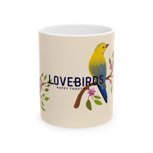 A cream-colored ceramic mug featuring a colorful illustration of a yellow and blue lovebird perched on a branch with pink blossoms and the text 'LOVEBIRDS HAPPY TOGETHER'.