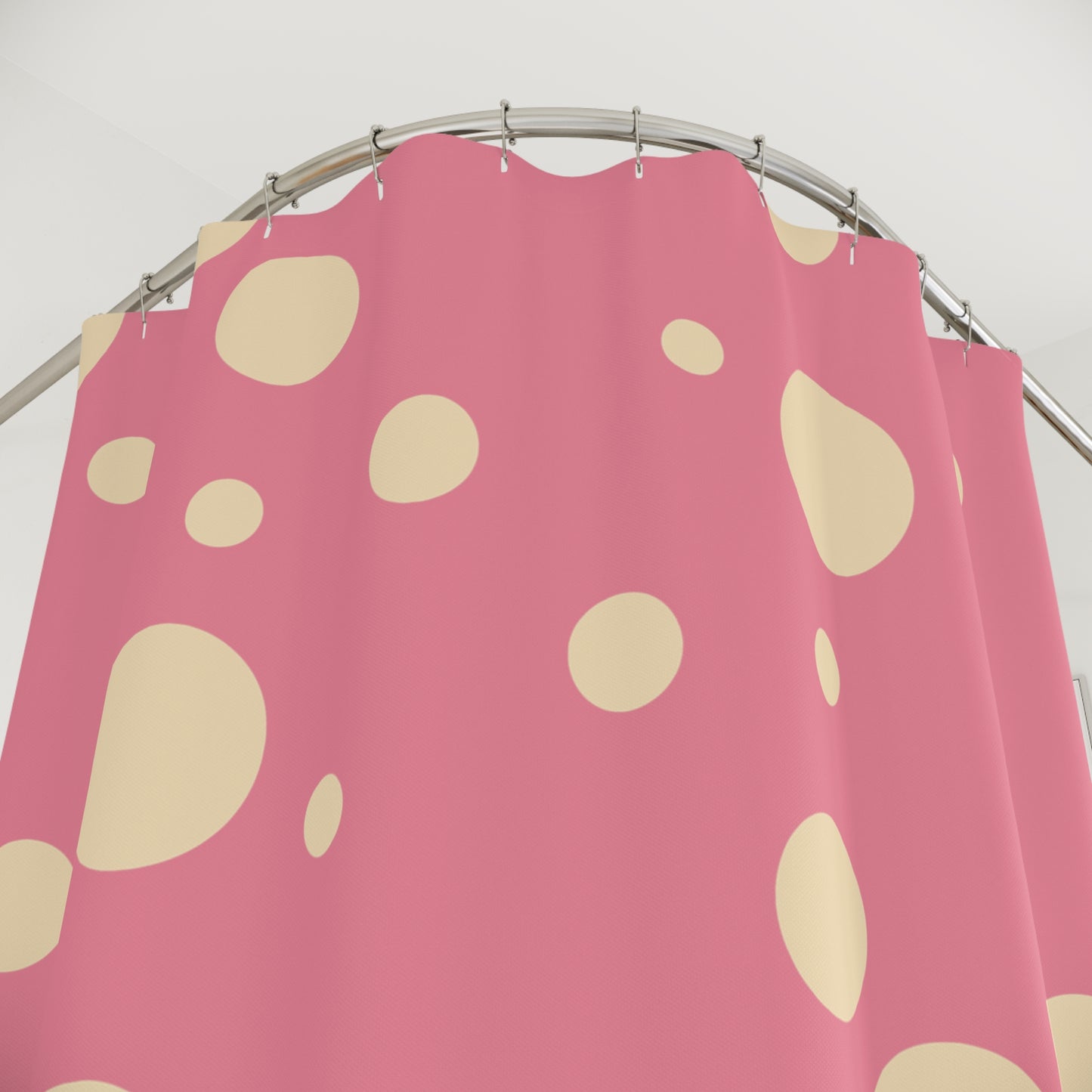 Pink shower curtain with irregular cream-colored spots, hanging from a curved silver metal rod against a plain light background.