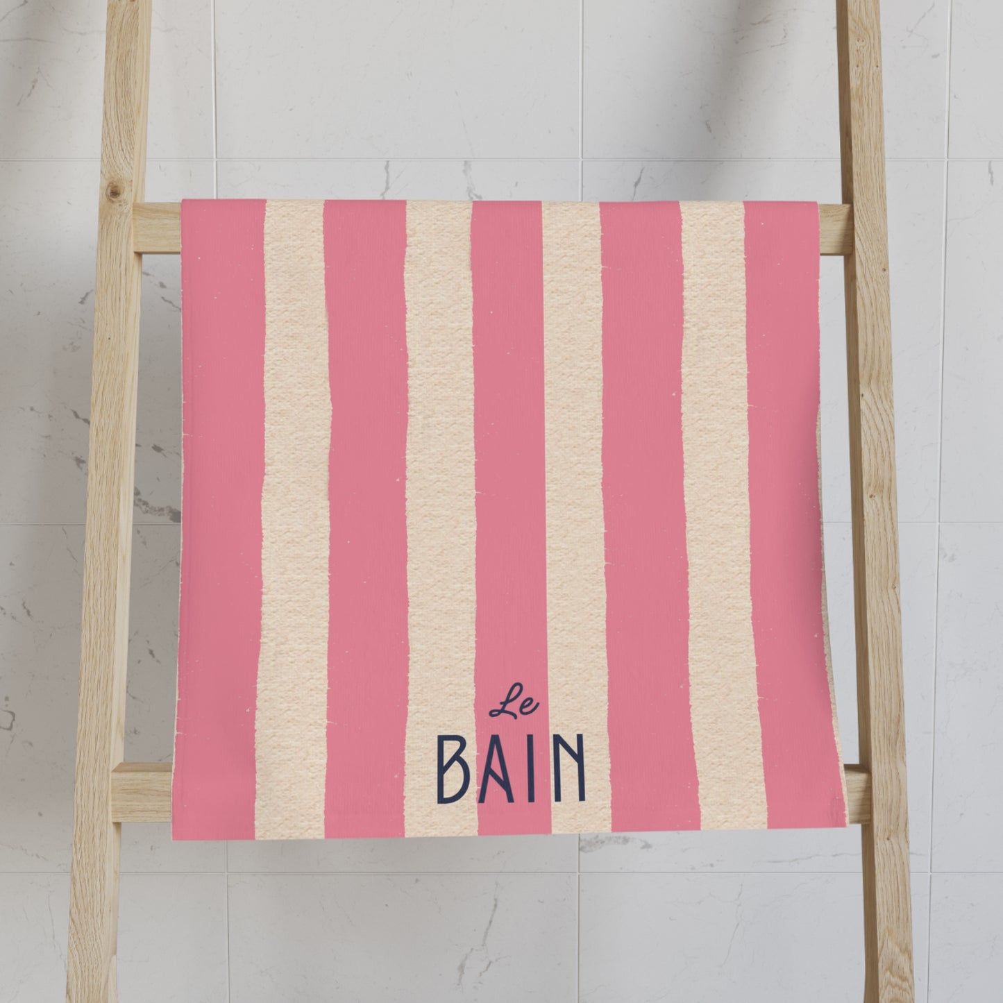 Pink and beige striped towel with 'Le Bain' text on a wooden ladder against a white wall.