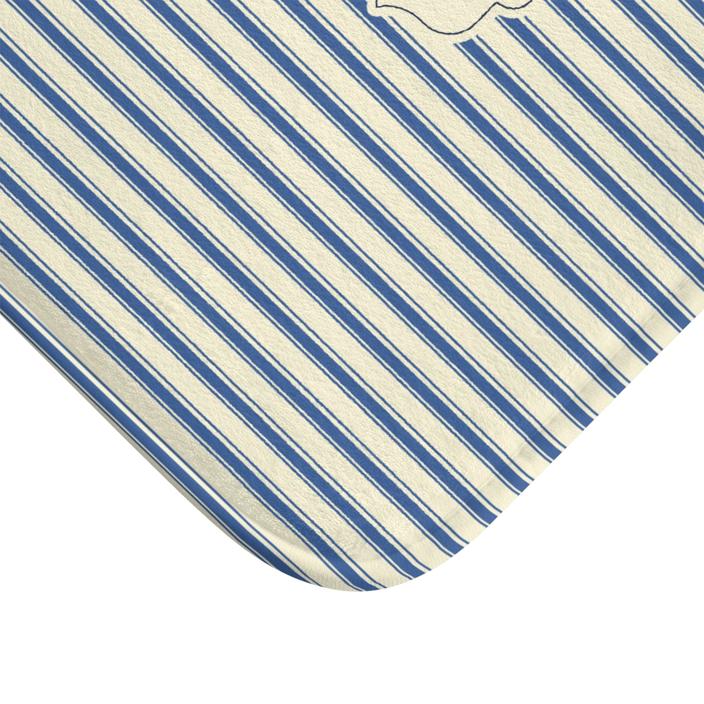 A close-up of a corner of a striped fabric item, showing diagonal blue and off-white stripes with a small embroidered monogram near the top edge, photographed on a white background.