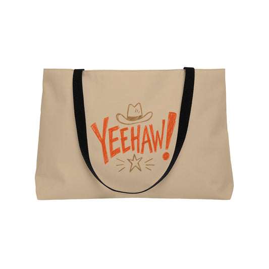 A beige canvas tote bag with black shoulder straps, featuring a retro-style orange 'YEEHAW!' graphic with a cowboy hat and star on the front, set against a plain white background.