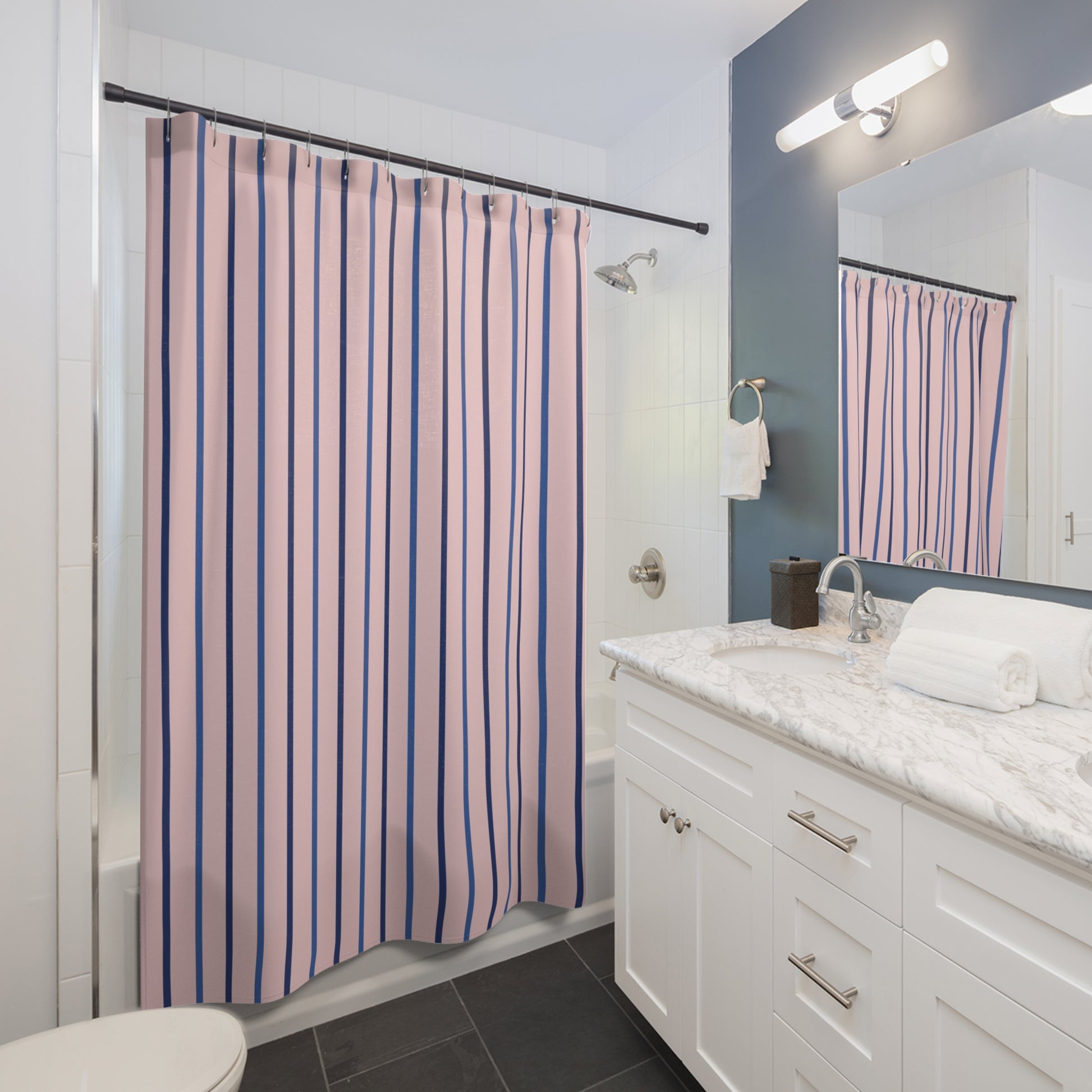 A pink and navy blue vertically striped shower curtain hanging in a modern white bathroom with a marble vanity, dark gray floor tiles, and a blue accent wall.