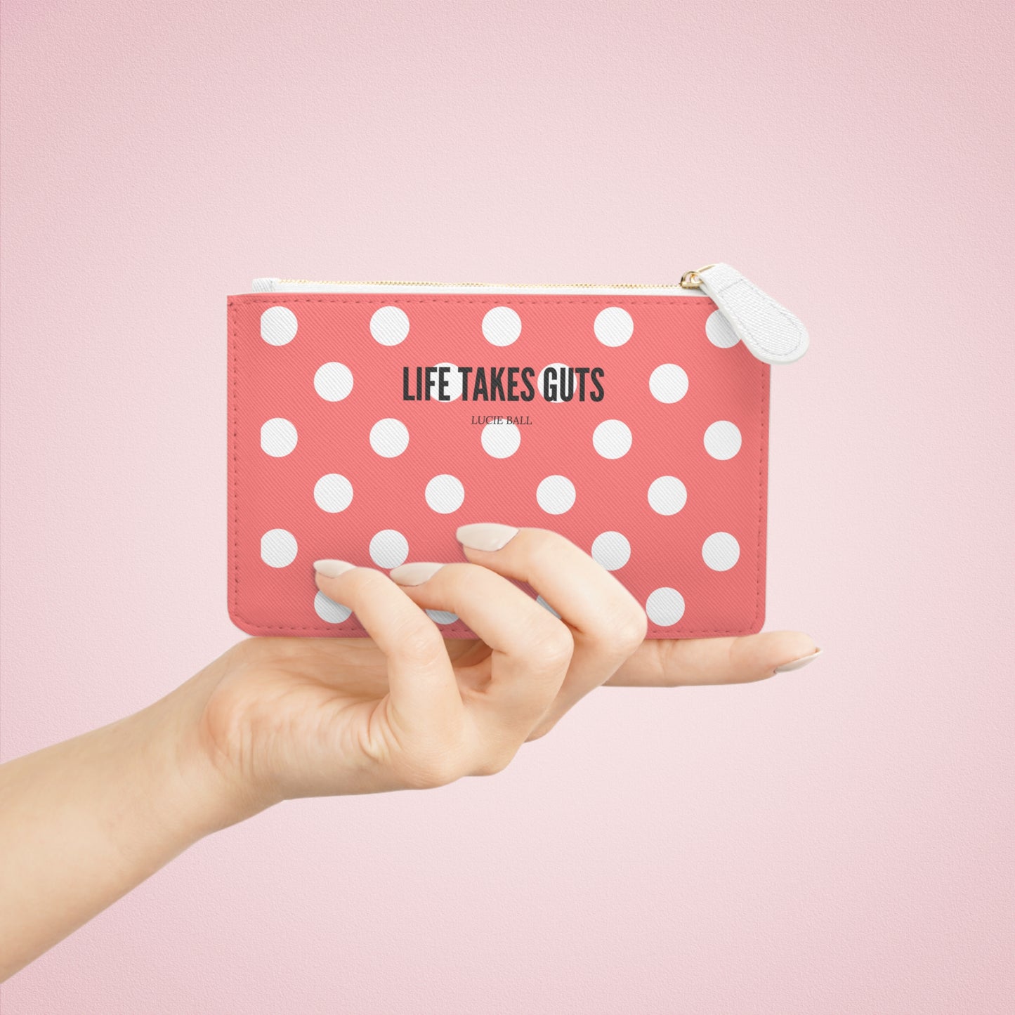 Pink polka dot pouch with 'LIFE TAKES GUTS' text held by a hand against a pink background