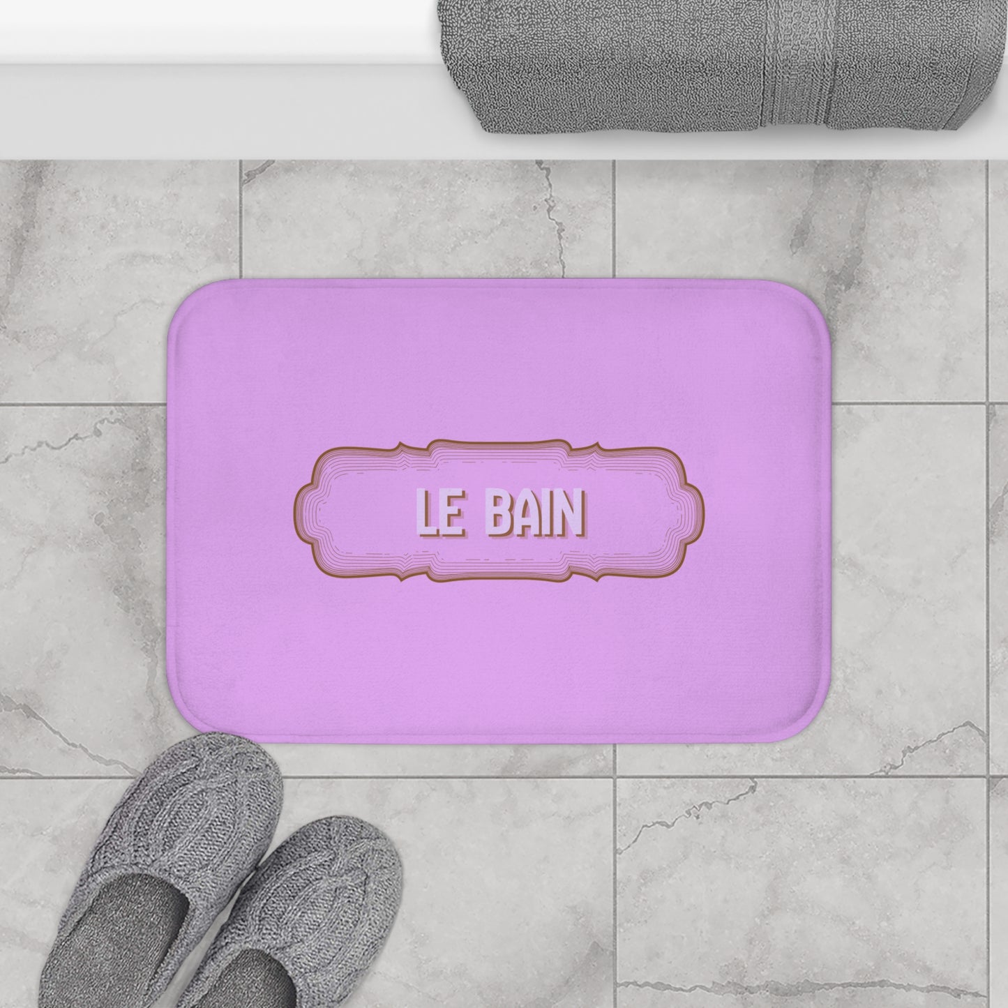Purple bath mat with 'LE BAIN' text on a marble floor with slippers and a towel.