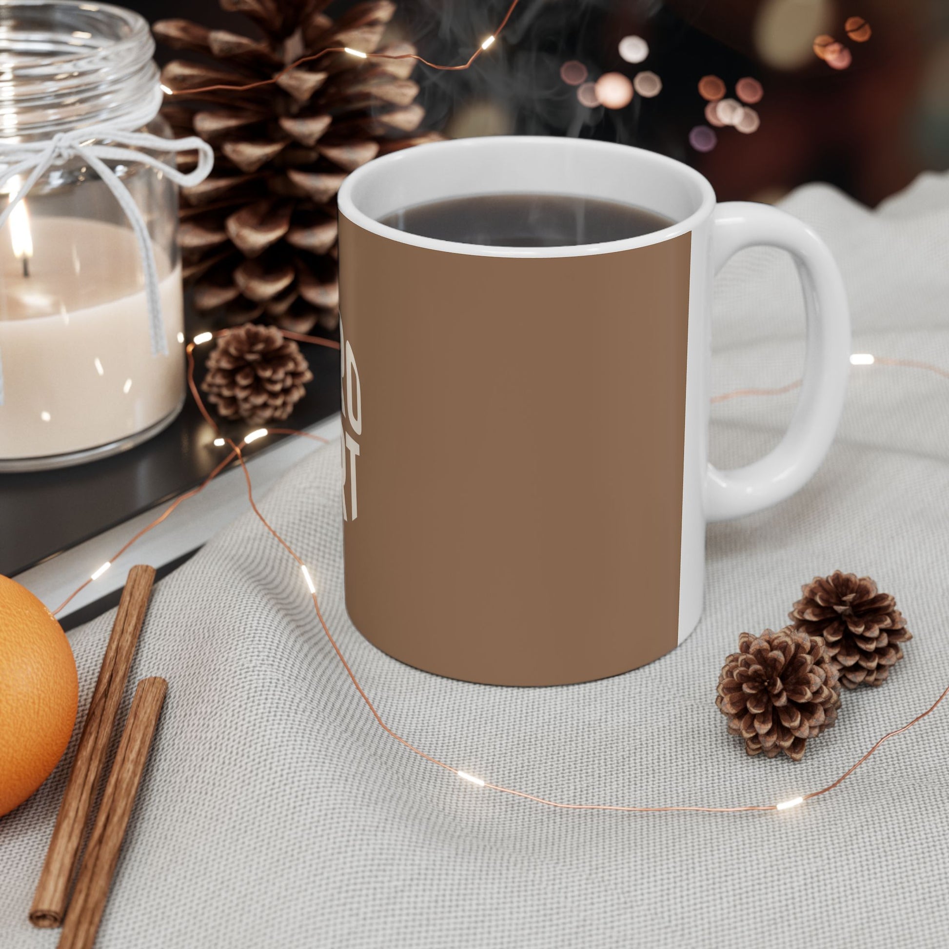 Brown mug with white handle on a table with decorative items like candles, pinecones, and an orange.
