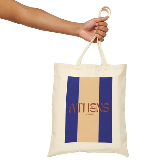 Tote bag with blue and beige stripes and 'Athens' text held by a hand on a white background