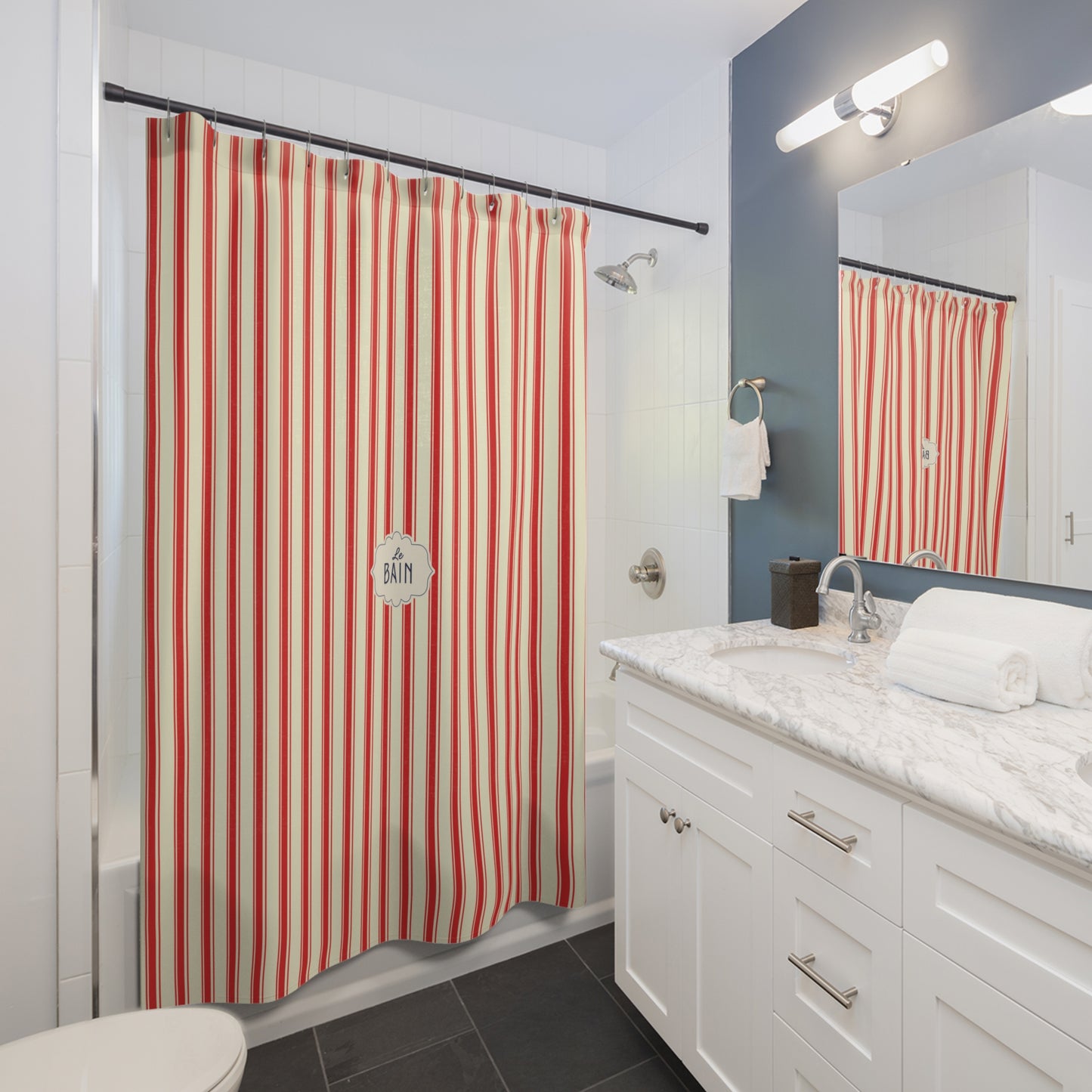 A bathroom scene showing a striped shower curtain in red, orange, and white, hanging in a bathtub next to a white vanity with a marble countertop and a mirror reflecting the curtain.