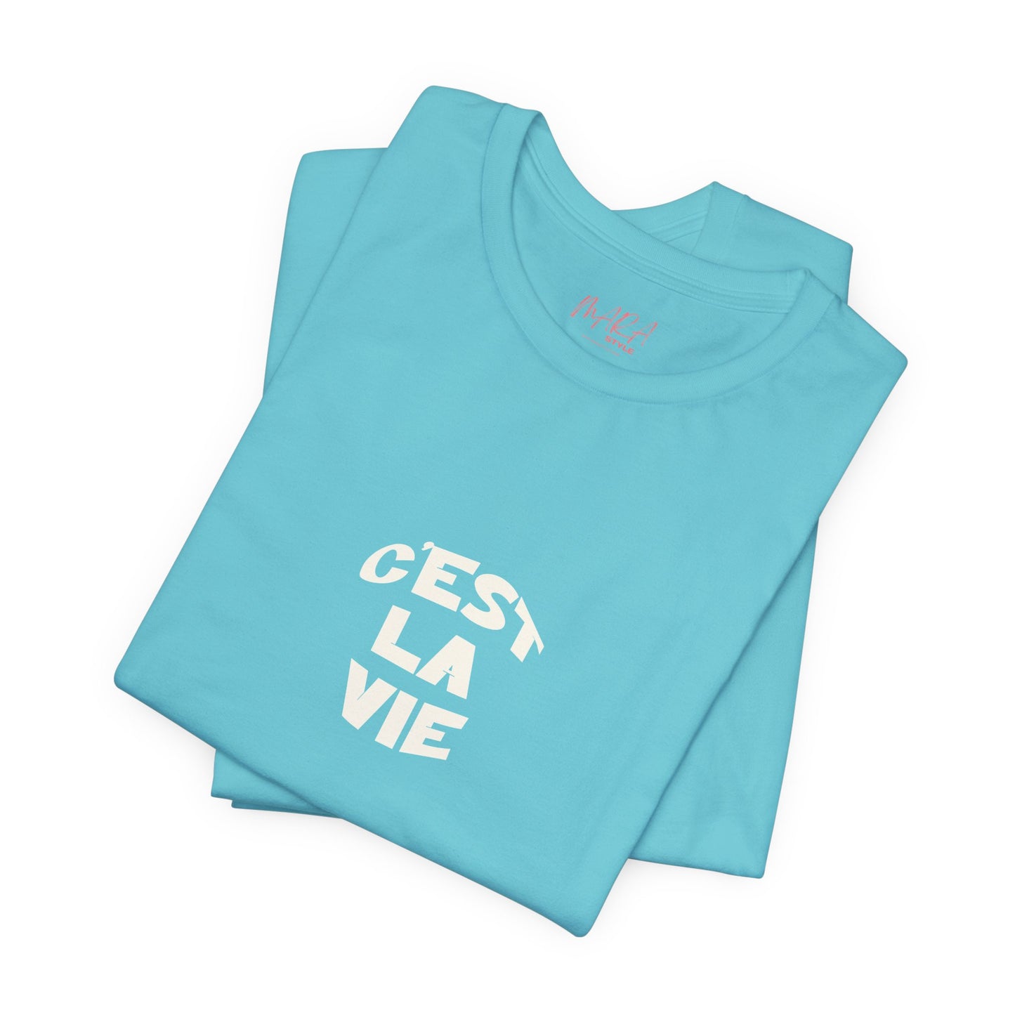 Folded light blue t-shirt with 'Cést La Vie' text on a white background