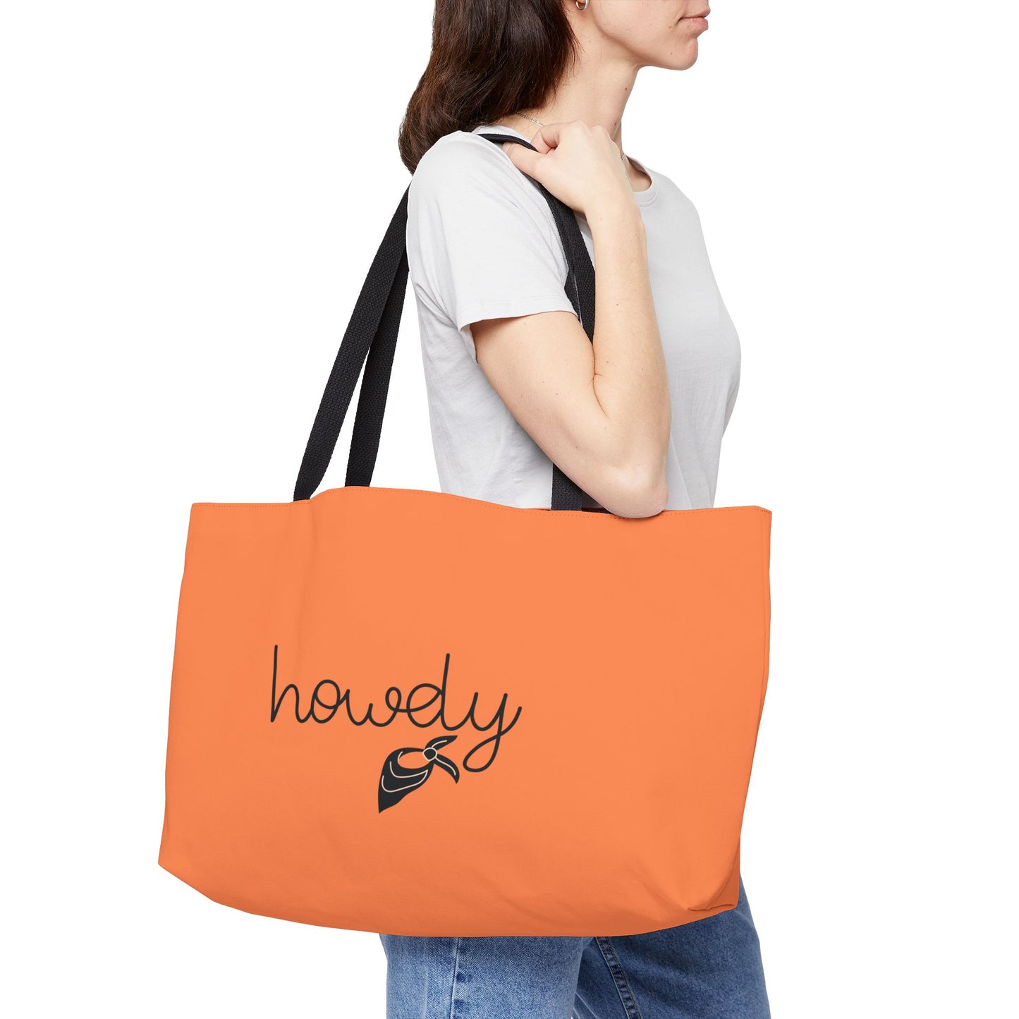 Person holding an orange tote bag with 'howdy' text and logo.