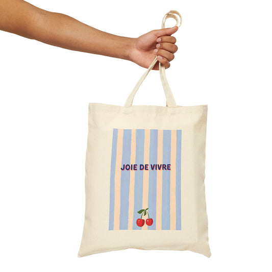 Tote bag with 'Joie de Vivre' text and cherry design held by a hand on a white background