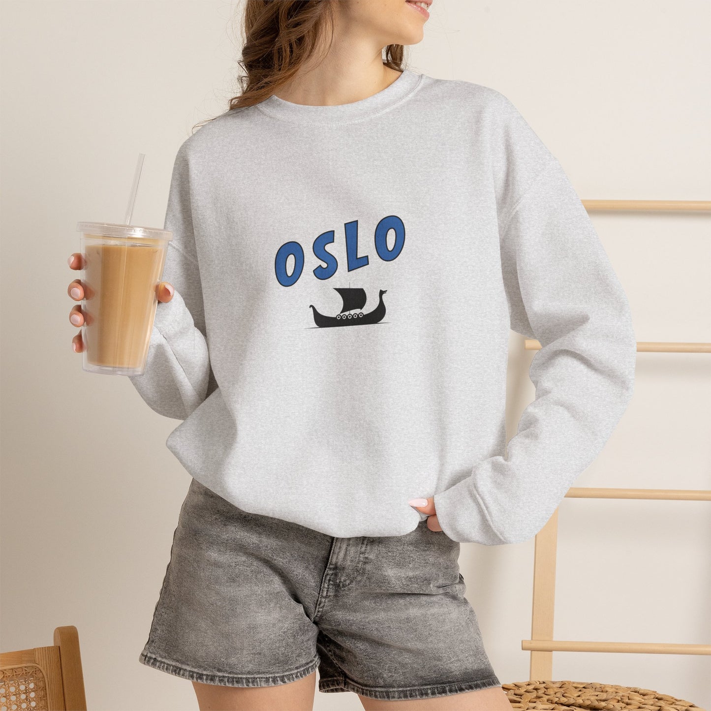 Person wearing a gray sweatshirt with 'OSLO' and a ship graphic, holding a drink.