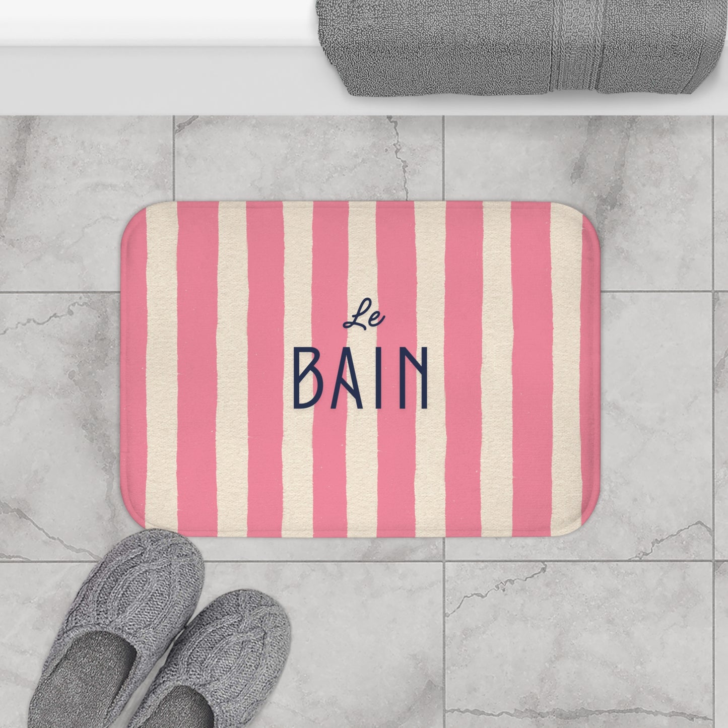 Striped bath mat with 'Le Bain' text on a tiled bathroom floor.
