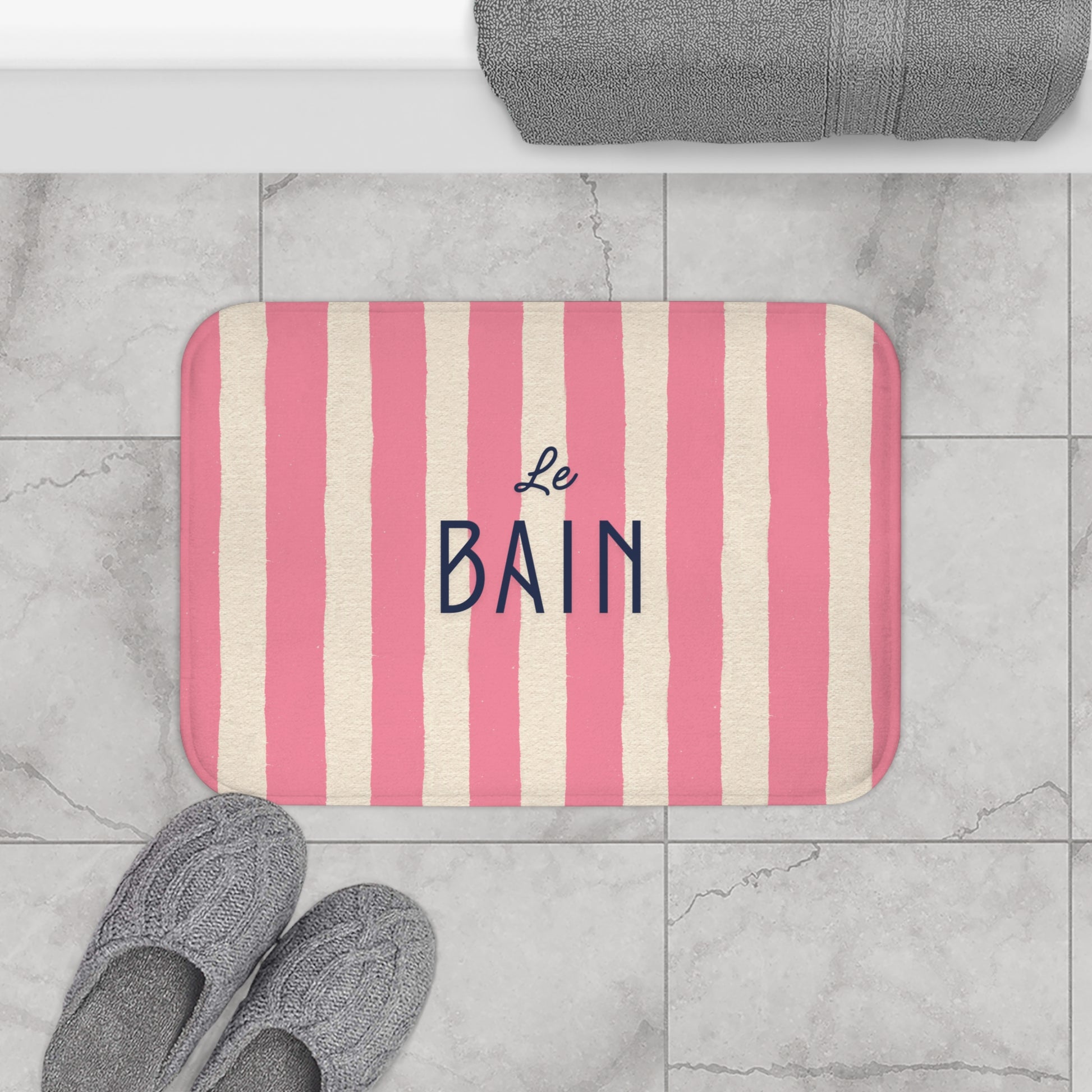 Striped bath mat with 'Le Bain' text on a tiled bathroom floor.