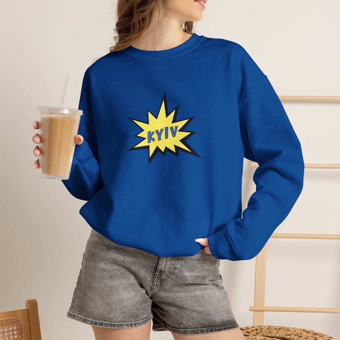 Person wearing a blue sweatshirt with a yellow 'KYIV' design, holding a drink.