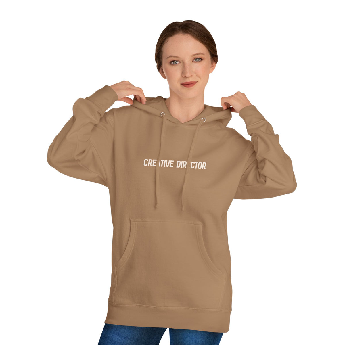 A woman wearing a tan pullover hoodie with 'CREATIVE DIRECTOR' printed in white text across the chest, shown against a plain white background.