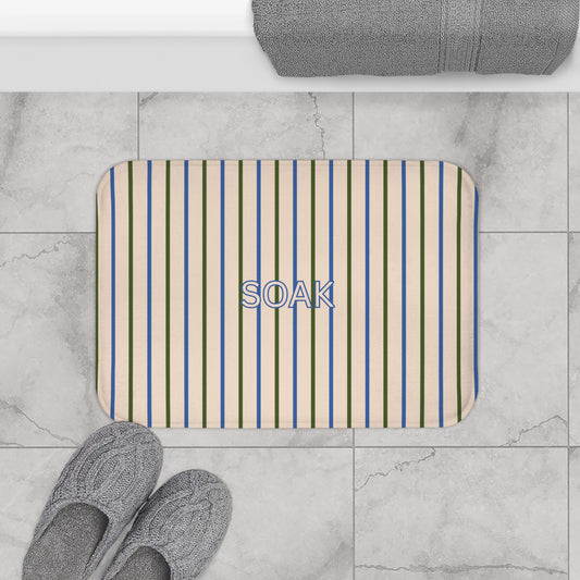 Striped bath mat with 'SOAK' text on a tiled bathroom floor.
