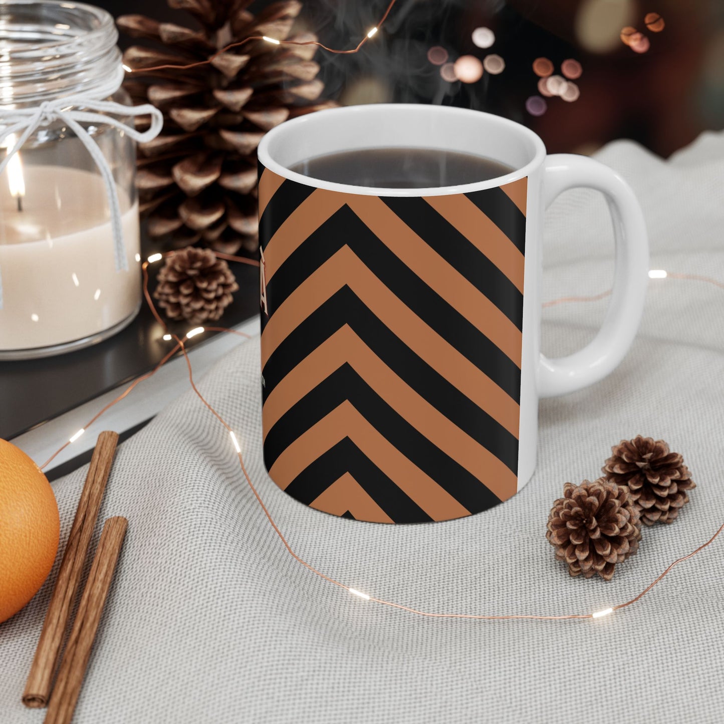 Mug with chevron pattern on a table with candles, oranges, and pinecones.