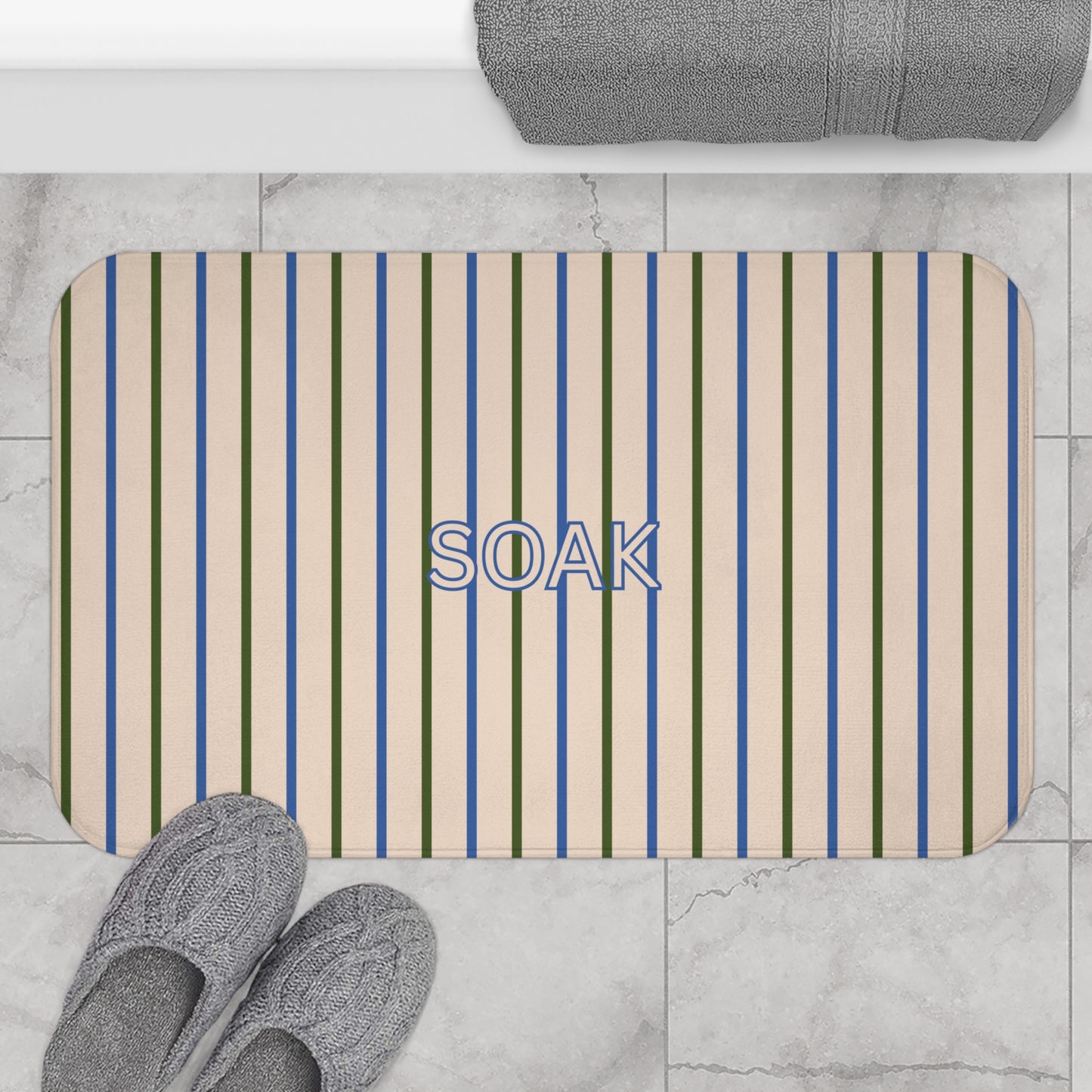 Striped bath mat with 'SOAK' text on a bathroom floor, surrounded by slippers and a towel.