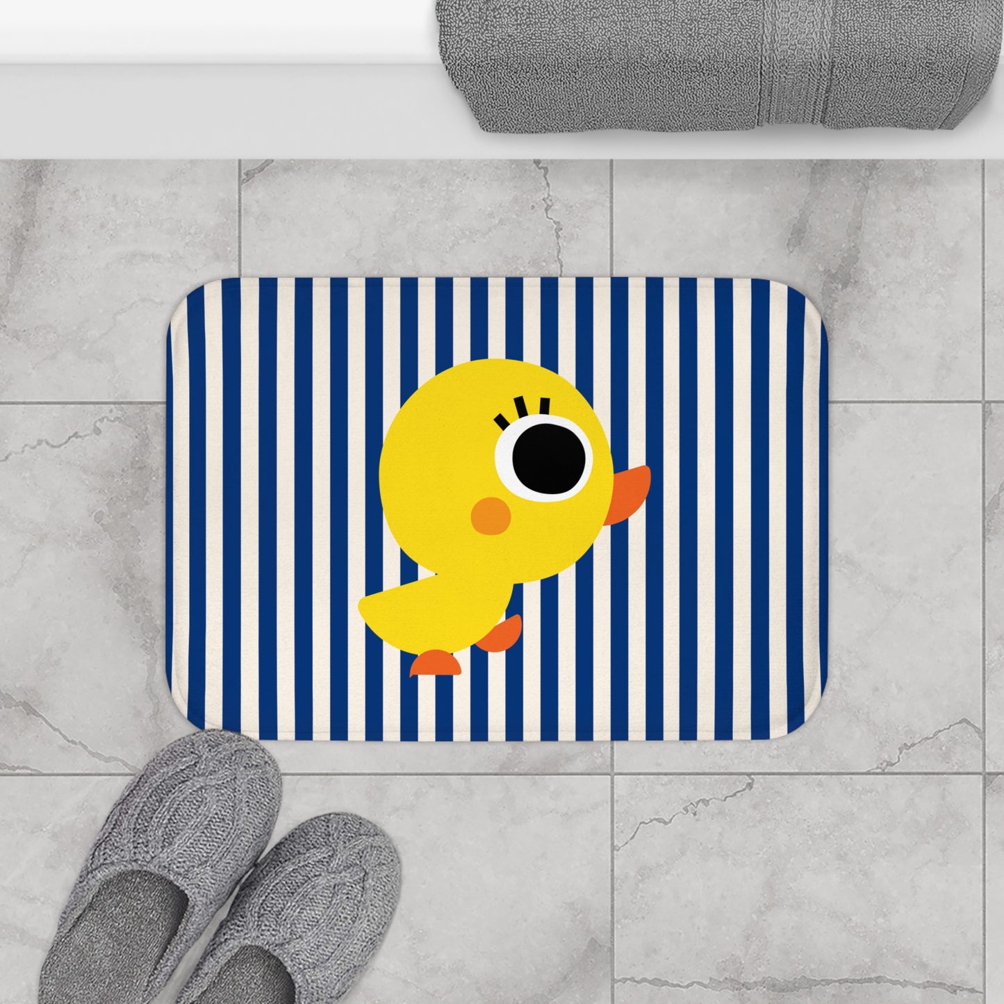 Bath mat with a yellow duck design on a blue and white striped background, placed on a tiled floor.