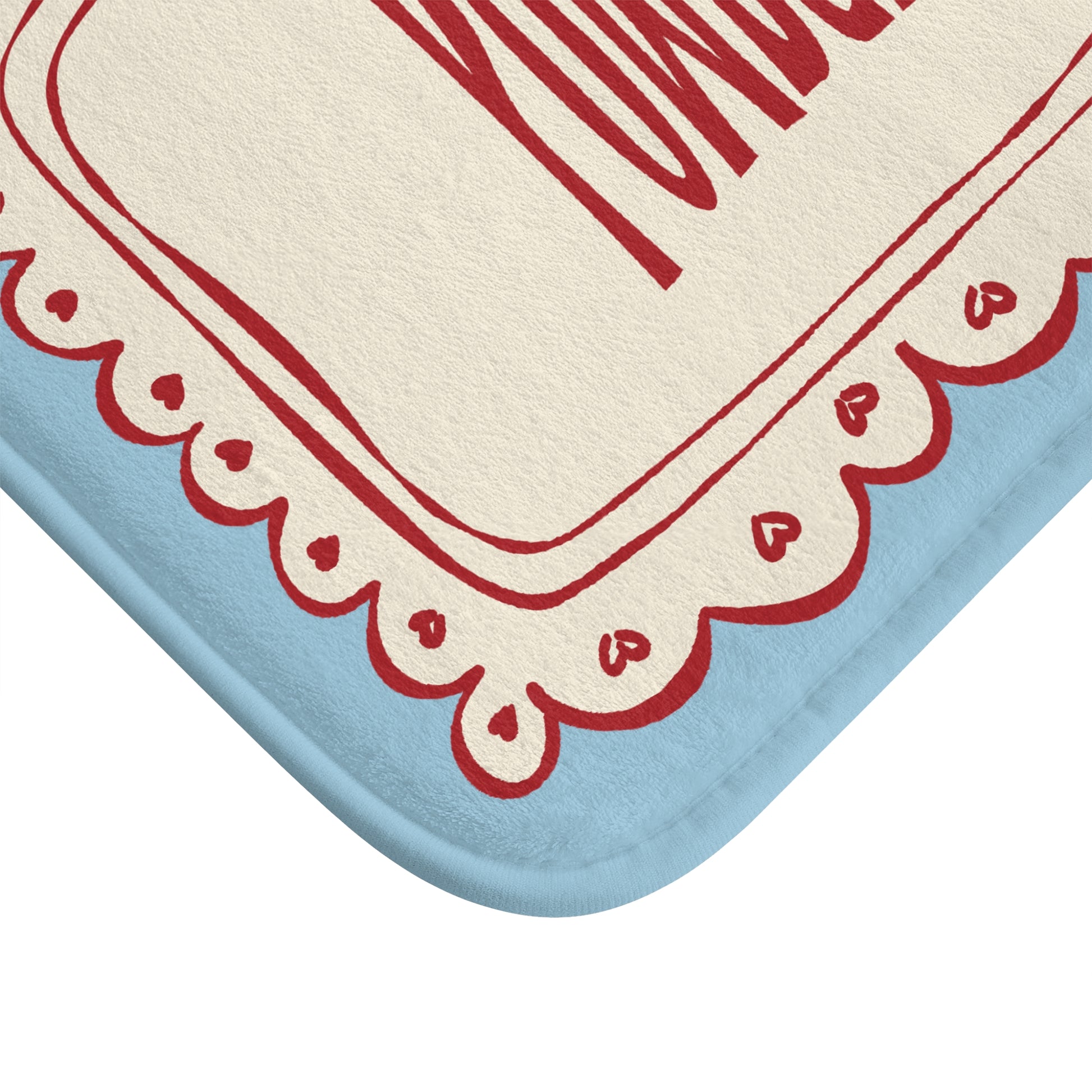 Decorative bath mat with red scalloped border and heart patterns on a blue and beige background