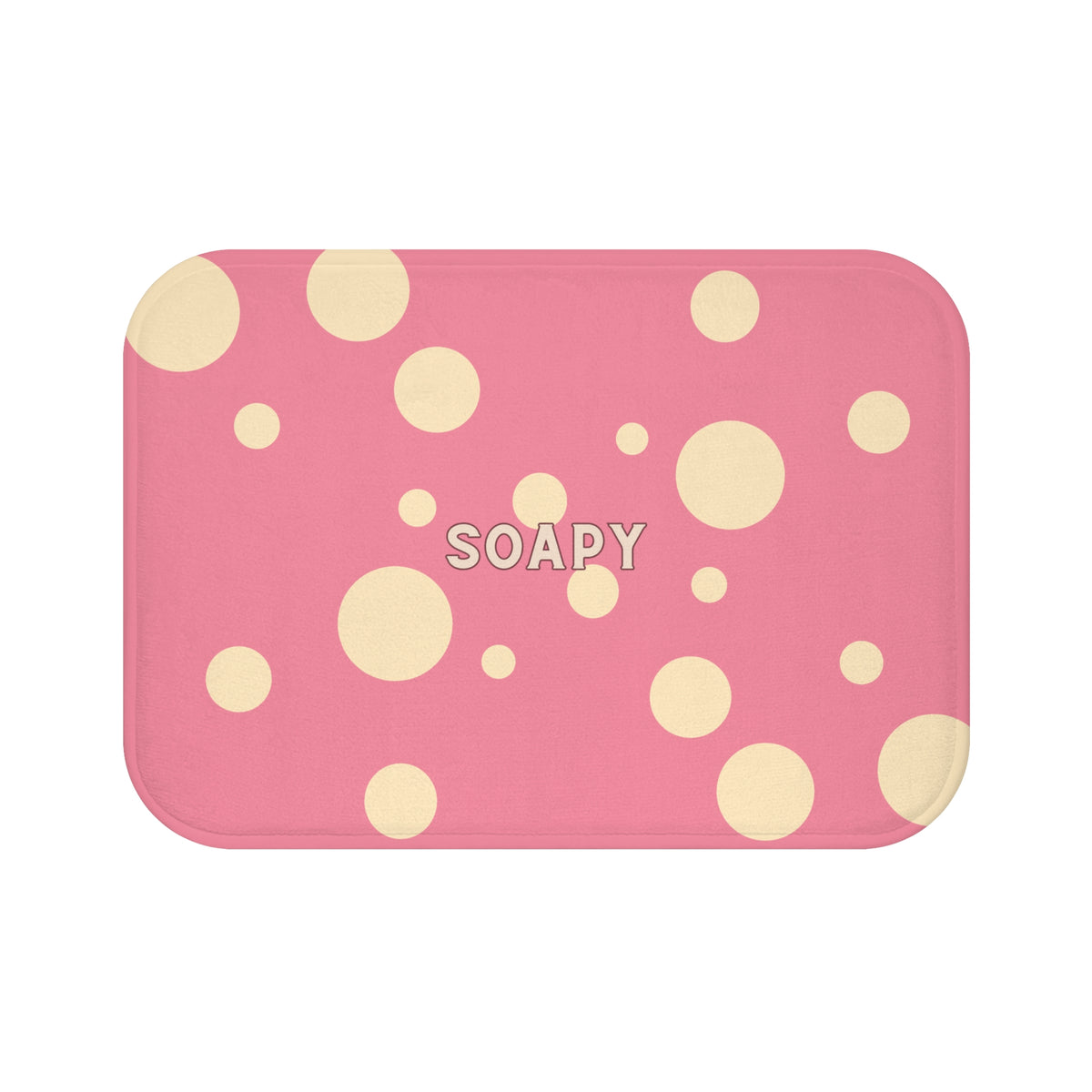 A rectangular pink bath mat with rounded corners, decorated with scattered cream-colored polka dots and the word 'SOAPY' printed in the center.