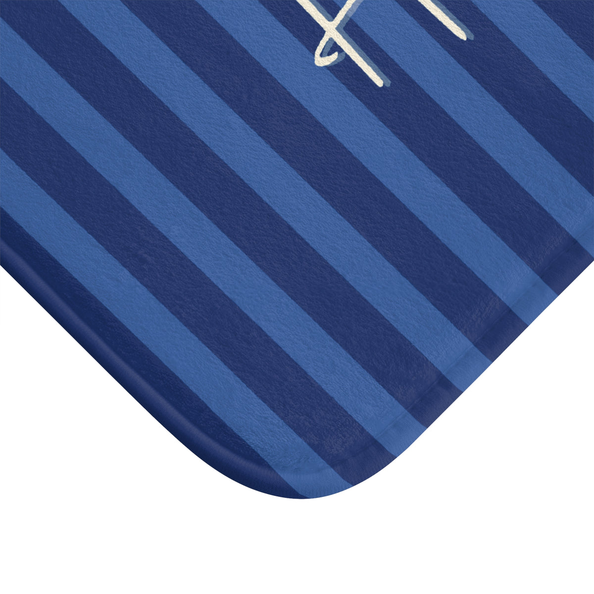 A close-up of a blue striped textile product corner with alternating medium and dark blue stripes and a small white embroidered letter near the top edge, shown on a white background.