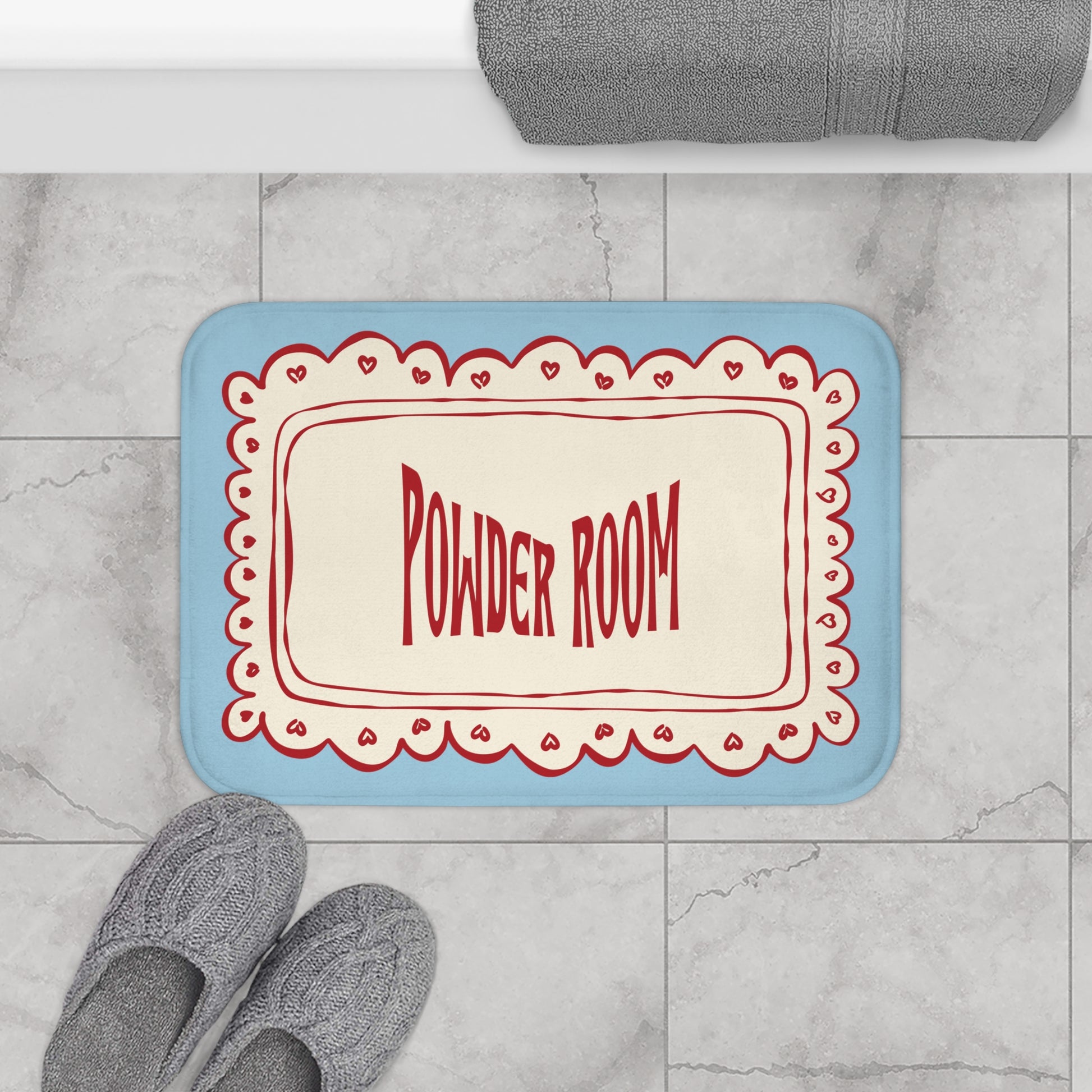 Doormat with 'Powder Room' text on a marble floor with slippers and a towel.