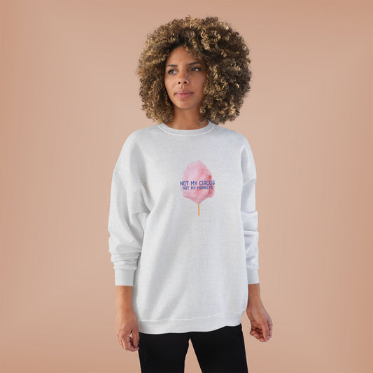 A woman with a large curly afro stands against a solid peach studio background wearing a light gray sweatshirt with a pink cotton candy graphic and the text 'NOT MY CIRCUS .