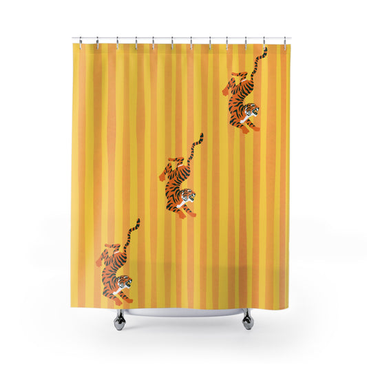 A yellow shower curtain with vertical orange stripes and three cartoon tigers walking diagonally across it, shown hanging over a white bathtub against a white background.