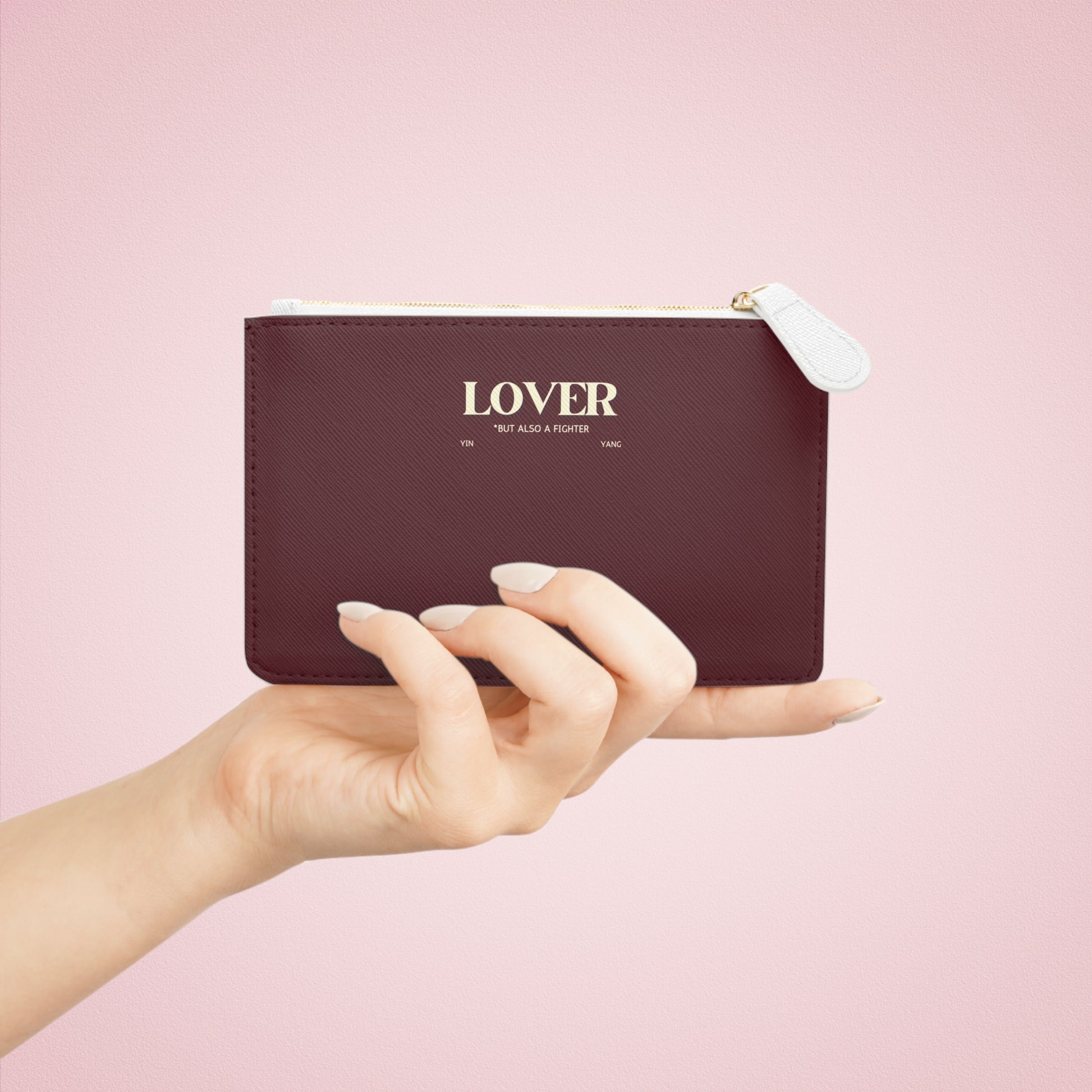 Hand holding a maroon pouch with 'LOVER' text on a pink background