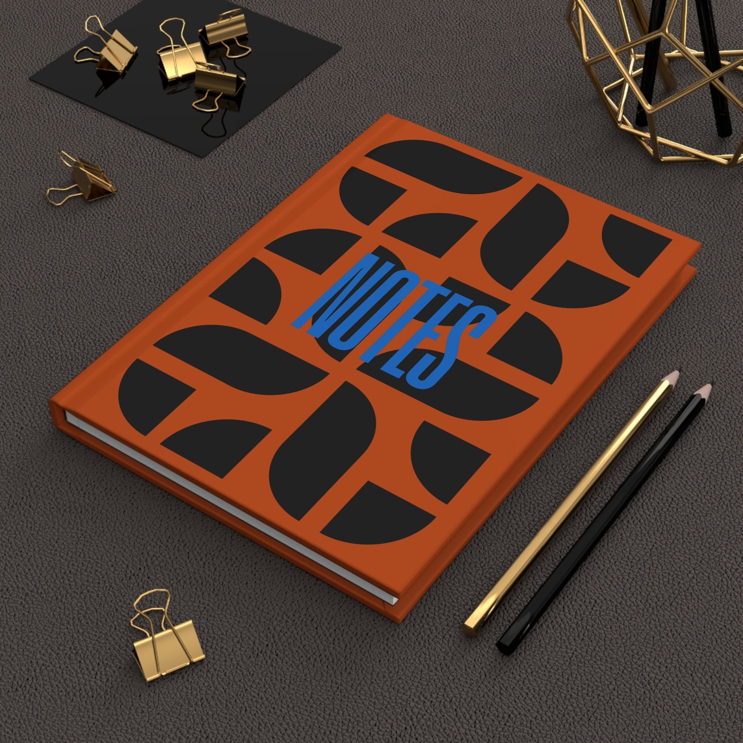 Notebook with decorative cover on a dark surface with office supplies.