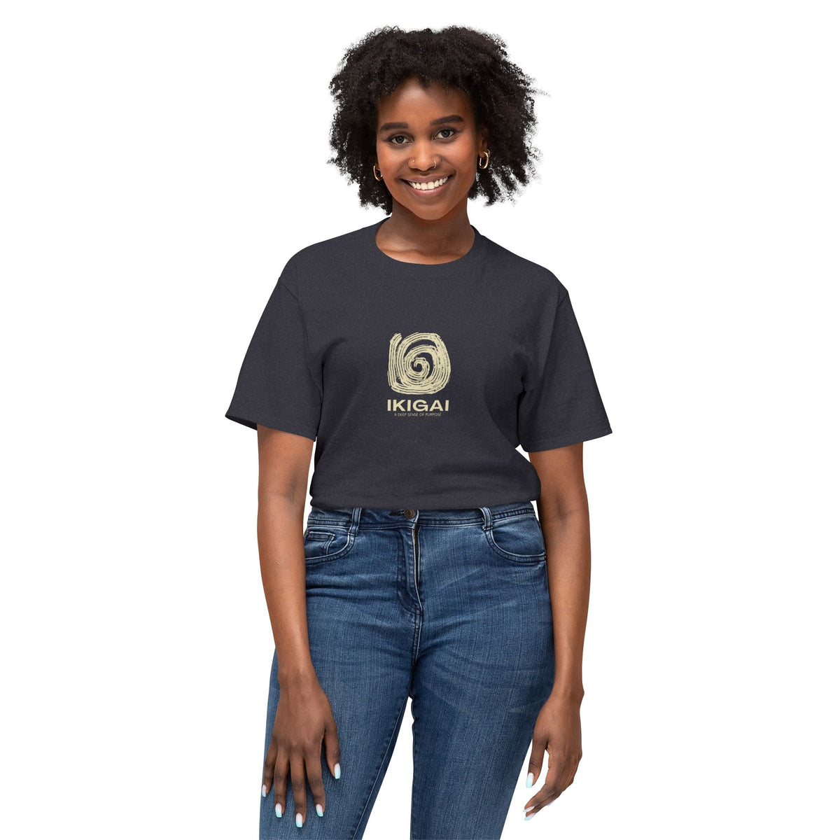 A woman with curly black hair wearing a dark charcoal gray t-shirt with a gold spiral logo and the word 'IKIGAI' printed on the chest, paired with blue jeans, against a plain white background.