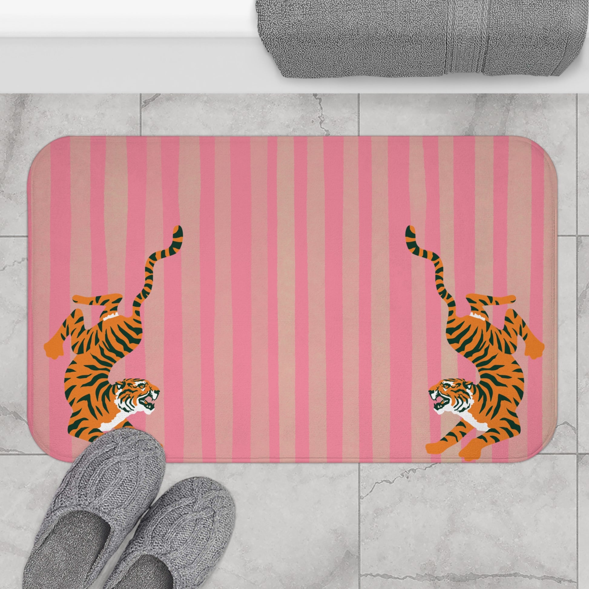 Bath mat with tiger design on a pink striped background, placed on a tiled floor.