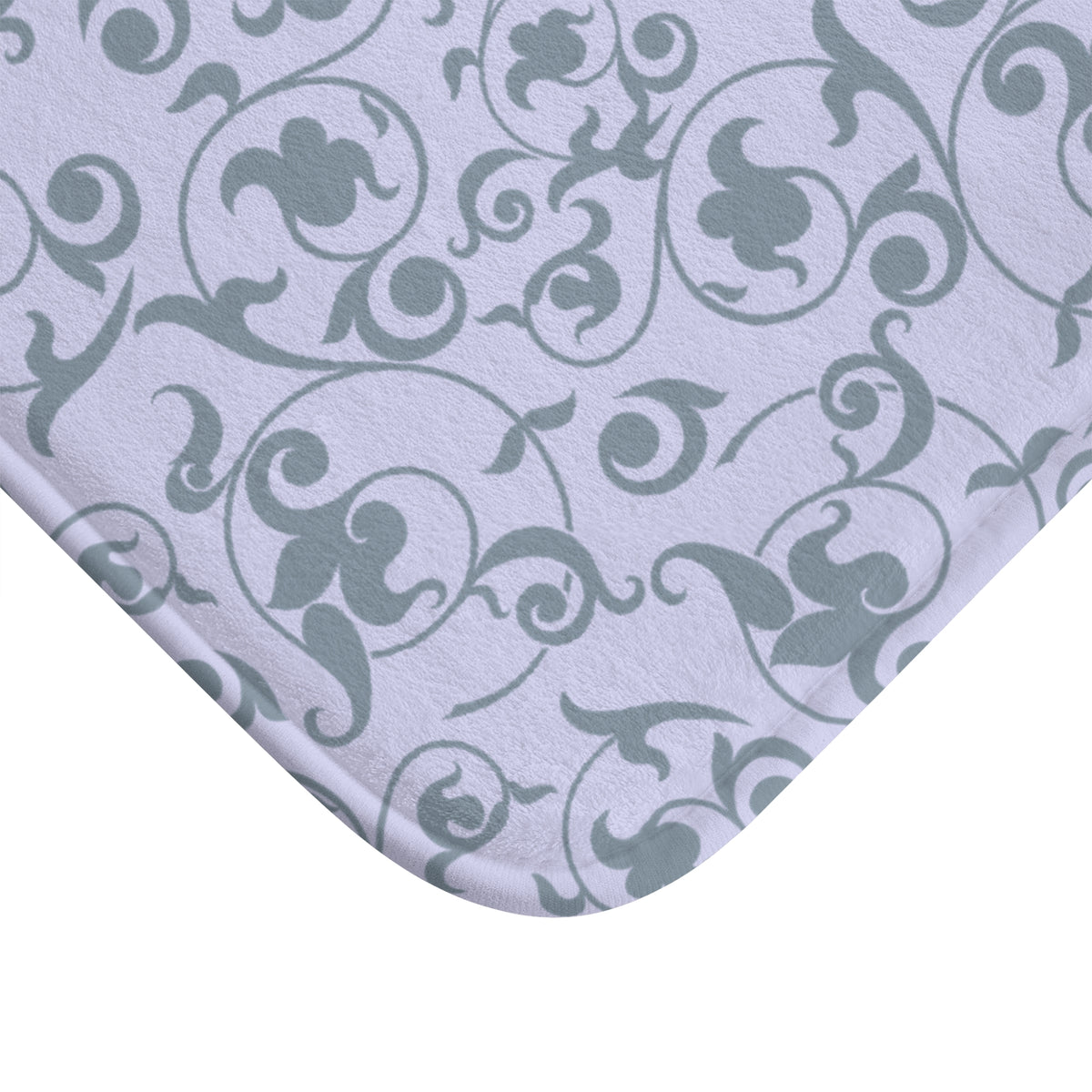 A close-up of a light lavender fabric with a gray damask scroll pattern, showing the corner of the material against a white background.
