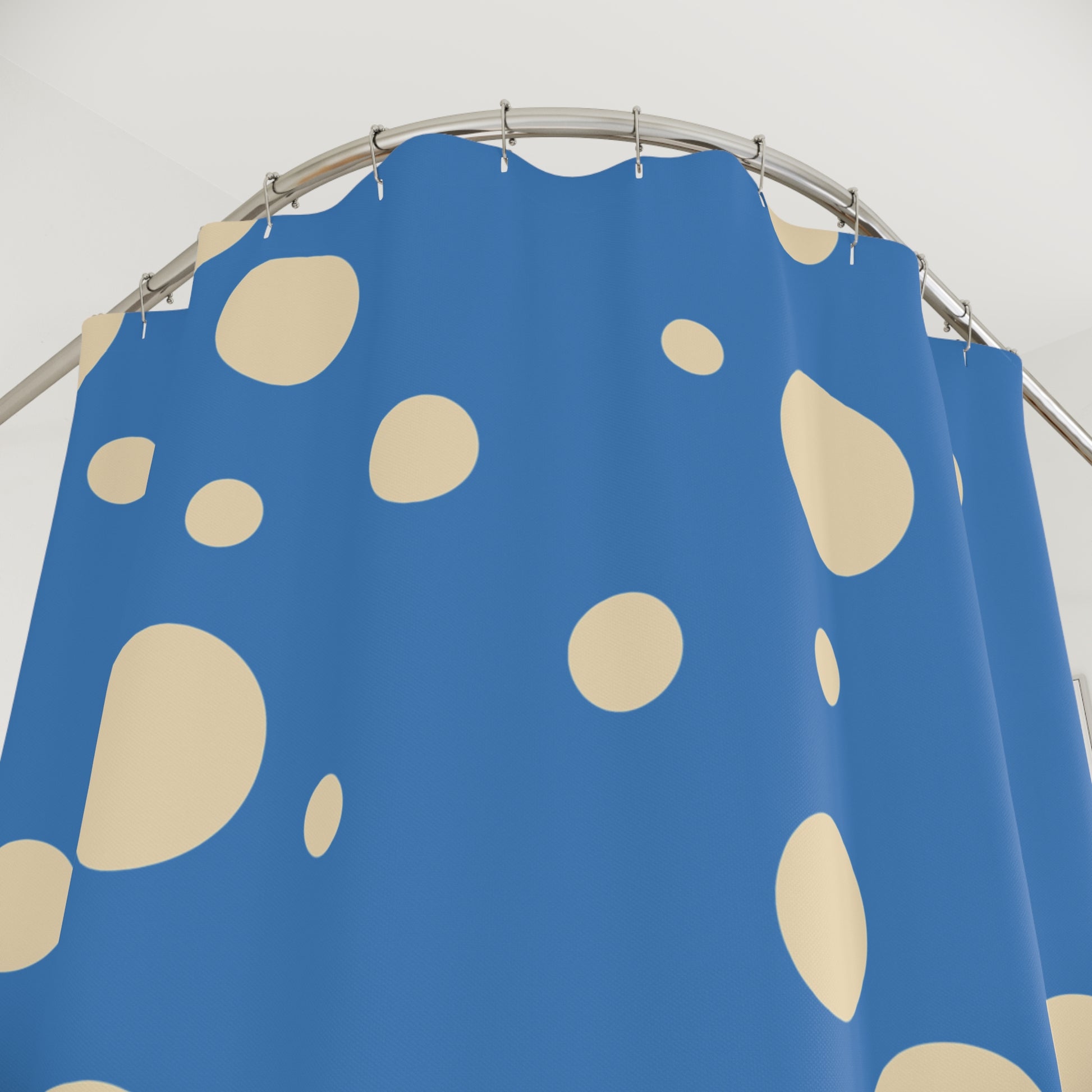 A blue shower curtain with a pattern of large beige spots, hanging from a curved silver metal rod against a plain light background.