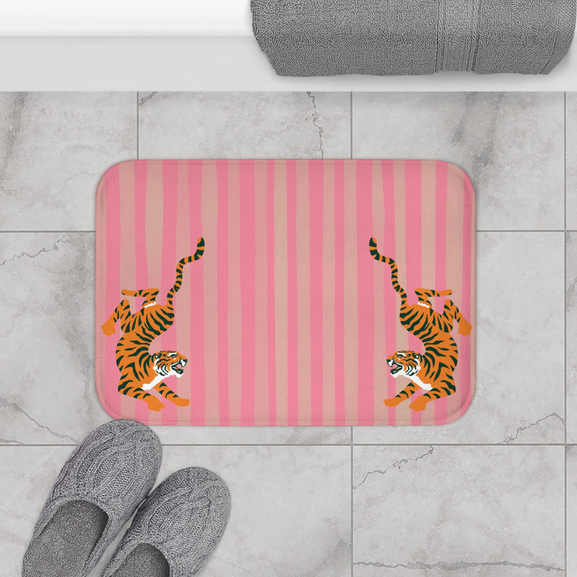 Pink striped bath mat with orange tigers on a marble floor.