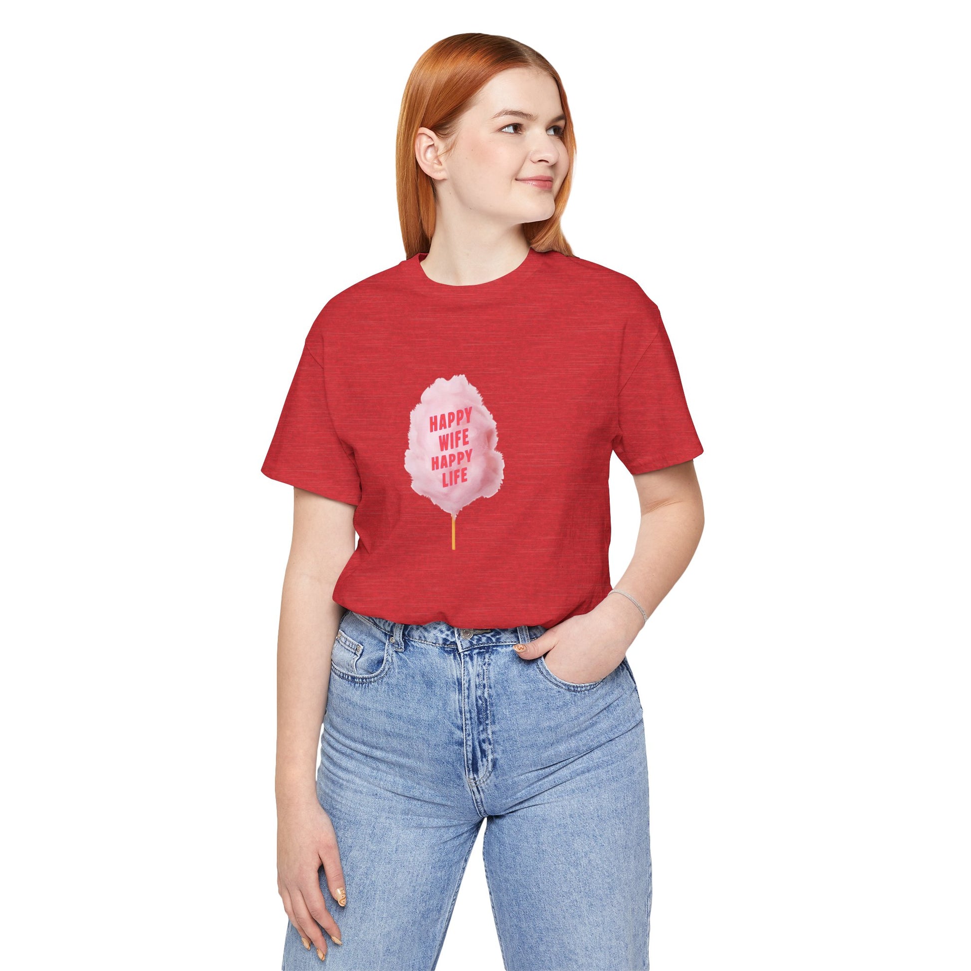 A woman with red hair wearing a heather red t-shirt with a pink graphic of a cotton candy leaf and the text 'HAPPY WIFE HAPPY LIFE', paired with light wash blue jeans, against a plain white background.