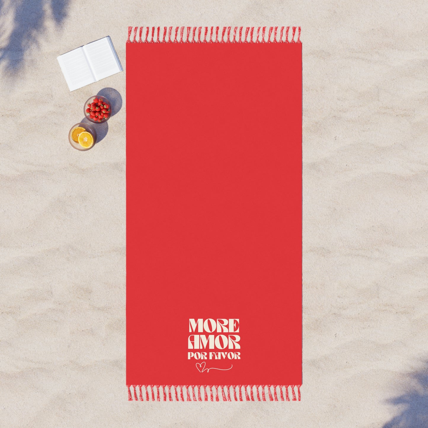 Red towel with 'More Amor Por Favor' text on a sandy surface