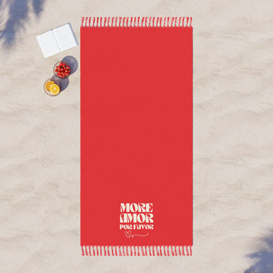Red towel with 'More Amor Por Favor' text on a sandy surface