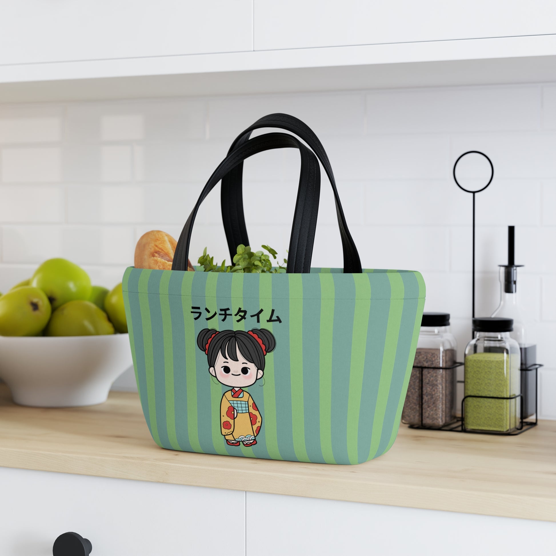 A green and light blue striped fabric lunch bag with black handles sits on a kitchen counter. The front features a cartoon girl in a kimono with Japanese text.