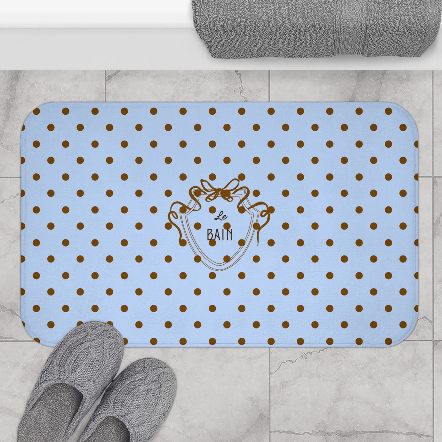 Blue bath mat with gold polka dots and a logo on a tiled floor.