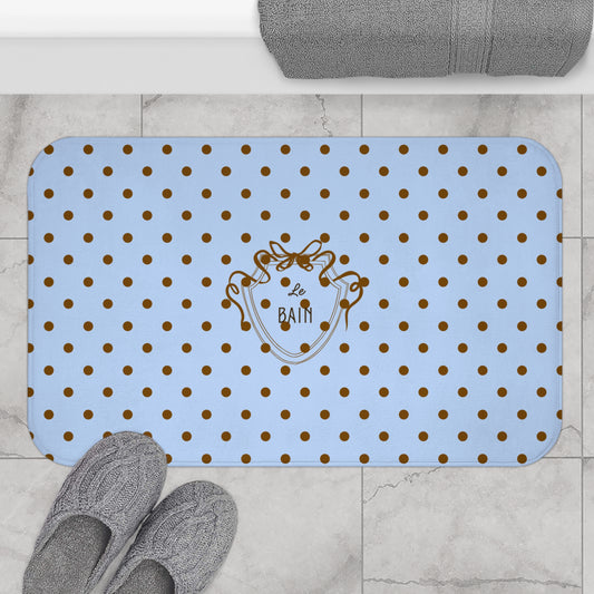 Blue bath mat with gold polka dots and a logo on a tiled floor.