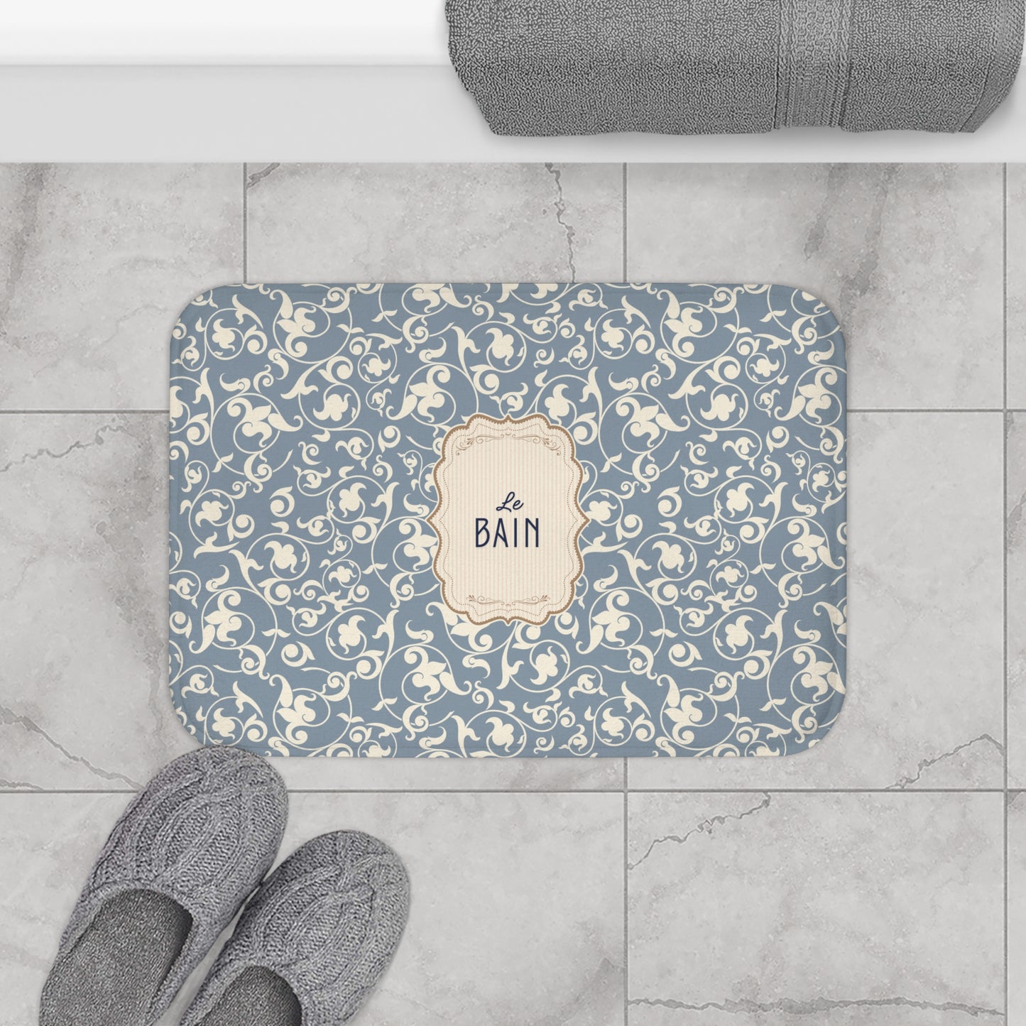 Decorative bath mat with floral pattern and 'Le Bain' text on a tiled floor.