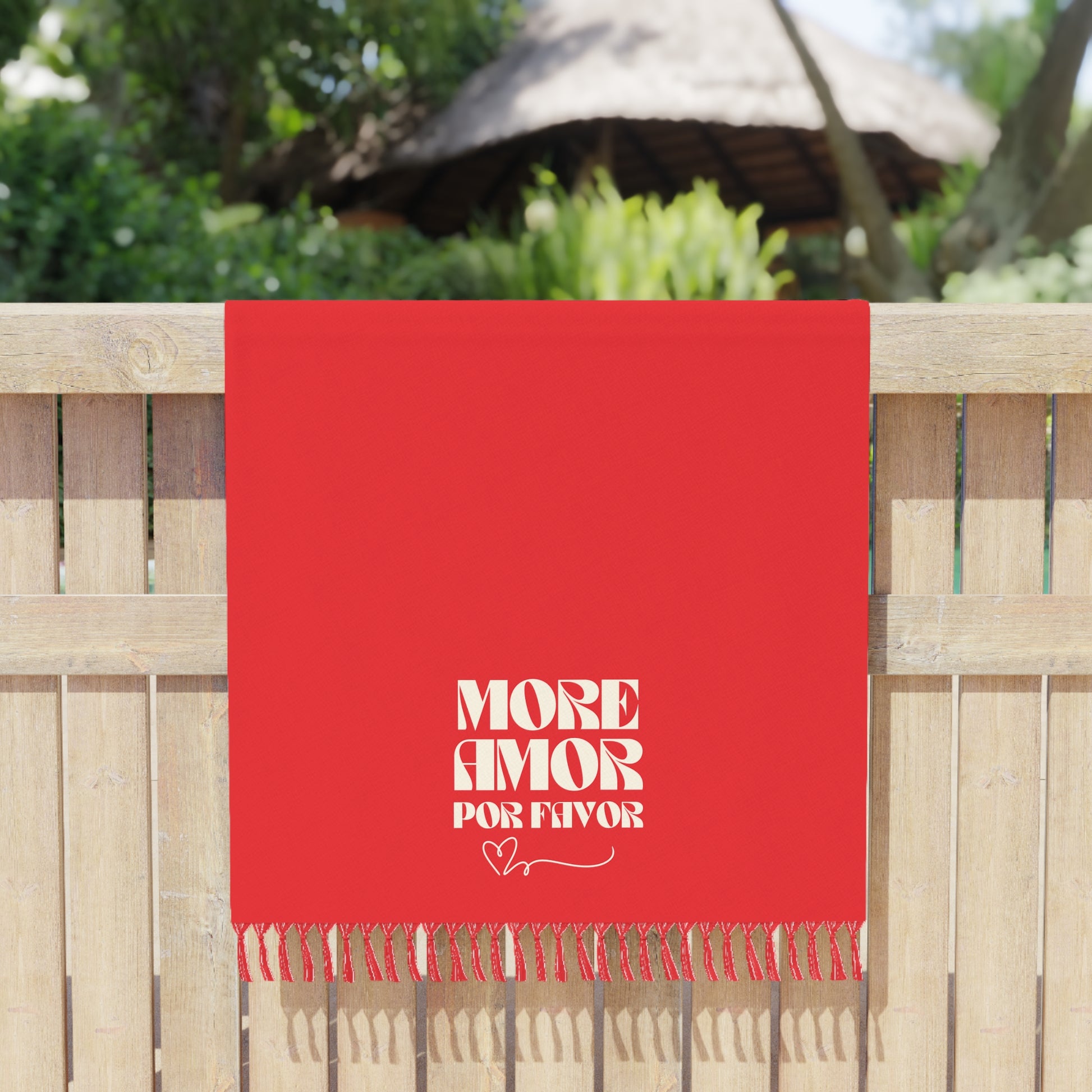 Red towel with 'More Amor Por Favor' text on a wooden fence