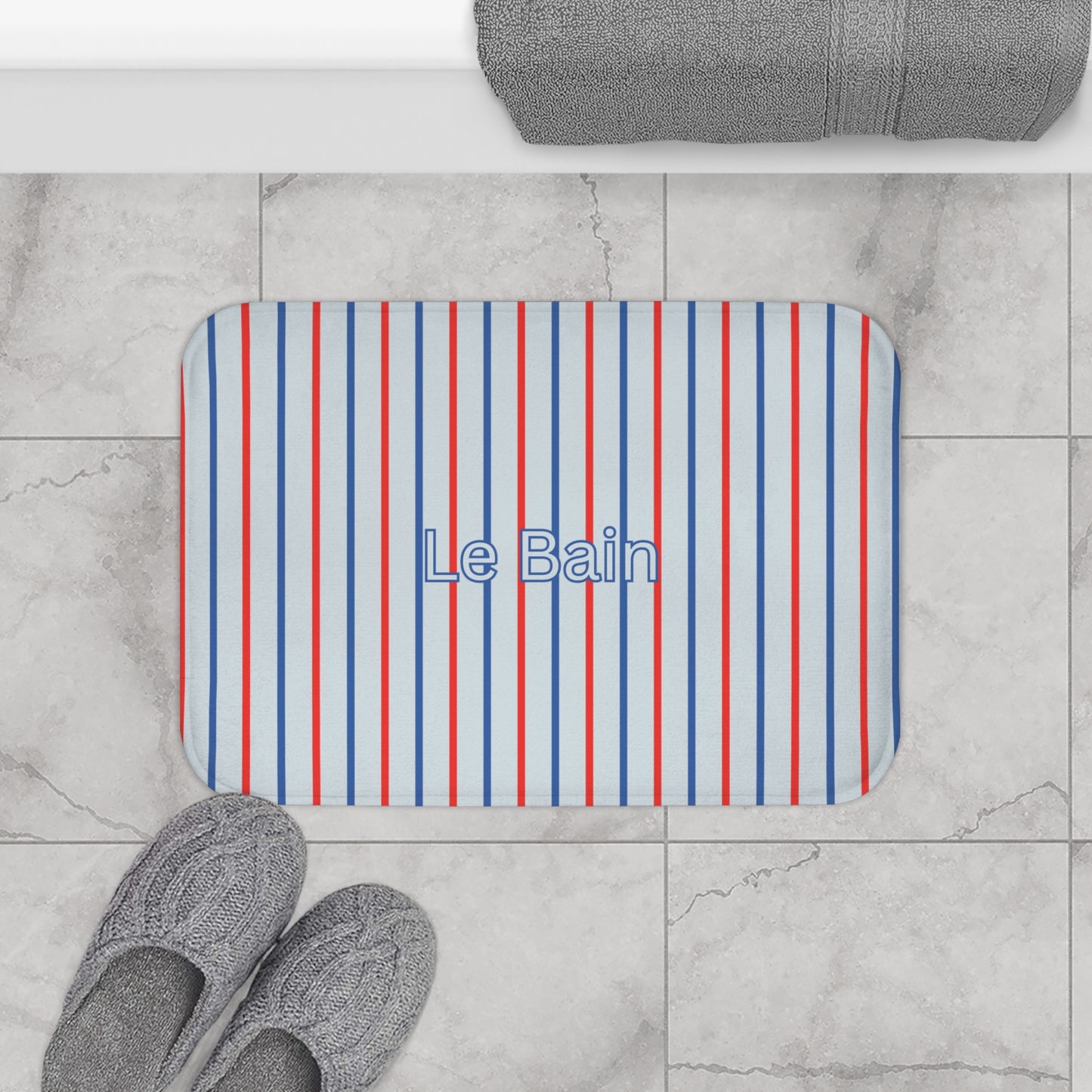 Striped bath mat with 'Le Bain' text on a marble floor with slippers and towel.