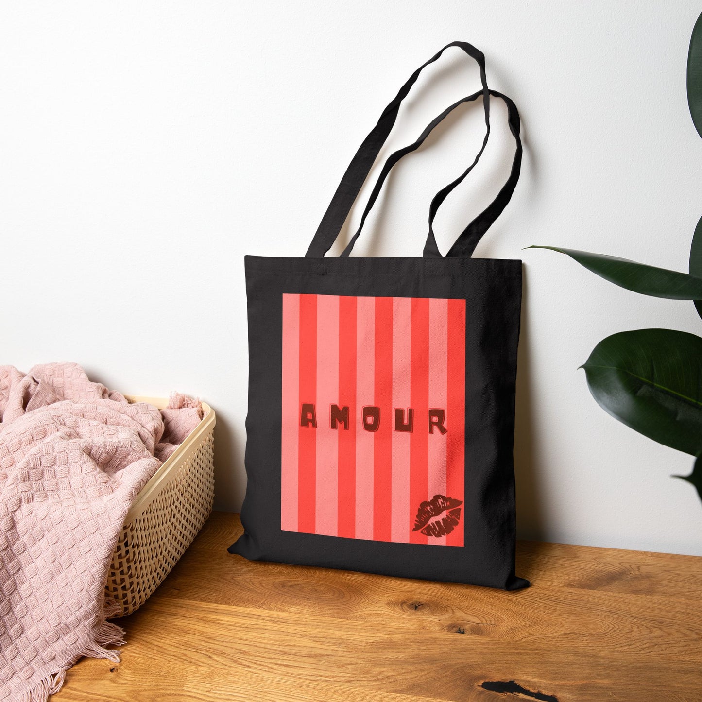 Black tote bag with red striped design and 'AMOUR' text on a wooden surface.
