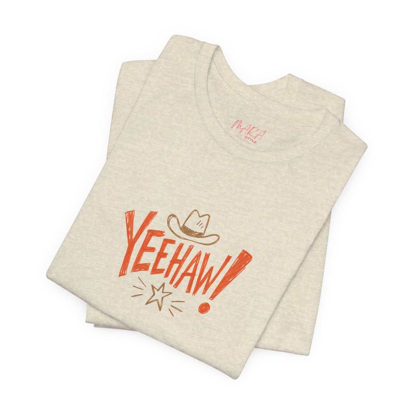 A folded light heather beige t-shirt with a western-themed graphic on the front. The graphic features the word 'YEEHAW!' in a bold orange-red font, a brown cowboy hat, and a small starburst detail.