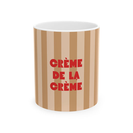 A cylindrical mug with vertical beige and light brown stripes, featuring the French phrase 'CRÈME DE LA CRÈME' printed in bold red letters on the front, set against a plain white background.
